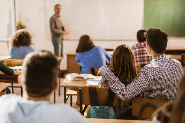 istock Back view of embraced high school couple attending a class in the classroom. 1326030677