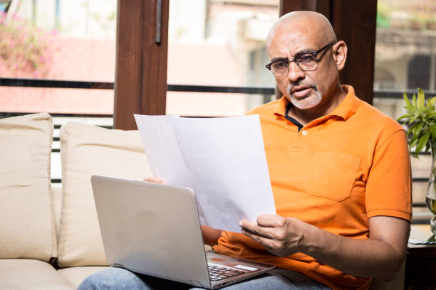 Middle age man in casuals working on laptop at home looking at the documents Middle age man in casual wear  working on laptop at home looking at the documents claim form stock pictures, royalty-free photos & images