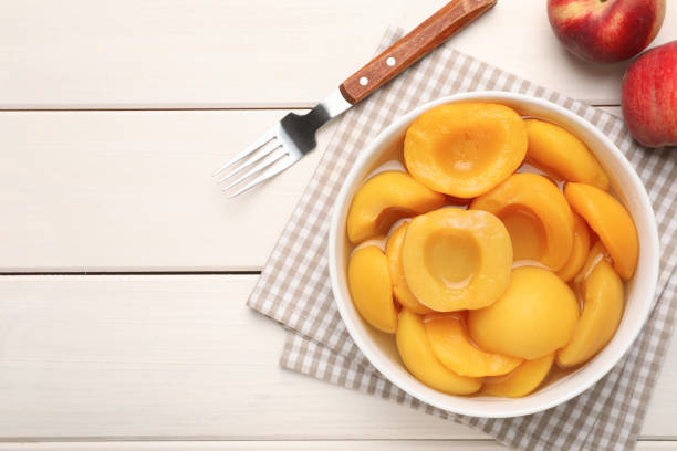 istock Canned peach halves and fork on white wooden table, flat lay. Space for text 1326032118