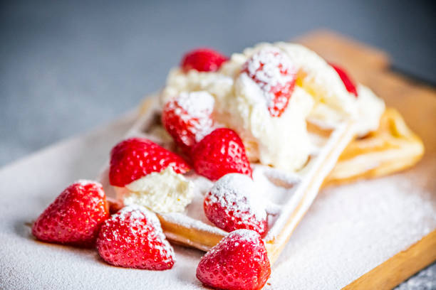 Waffles with strawberries and whipped cream.  Stack of pancakes in the background with raspberries and blueberries.  