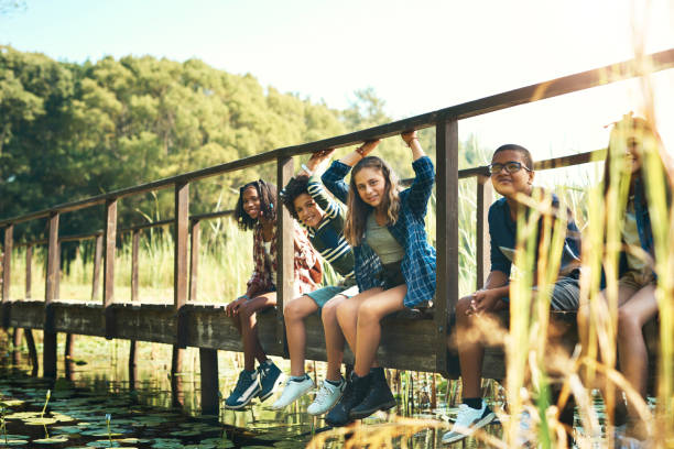 scatto di un gruppo di adolescenti seduti su un ponte nella natura al campo estivo - colonia estiva foto e immagini stock