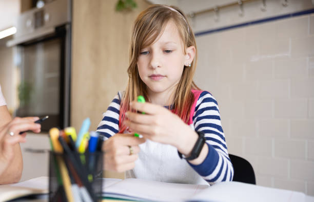 istock Elementary age girl looking at her pen, distracted from homework 1326033369