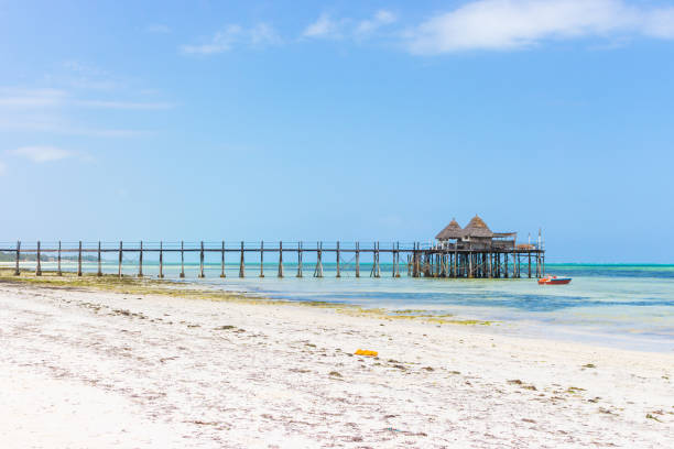 Wooden pier with boat and beach hut on sunny day. Low tide of Indian Ocean. Idyllic exotic resort. Pier in perspective with bungalows. Tropical paradise. Honeymoon in lagoon. Scenic tranquil seascape. Beach hut on island. Summer travel. muelle de madera con barco y cabaña de playa en día soleado. marea baja del océano Índico. idílico complejo exótico. muelle en perspectiva con bungalows. paraíso tropical. luna de miel en laguna. paisaje marino tranquilo y pintoresco. cabaña de pla