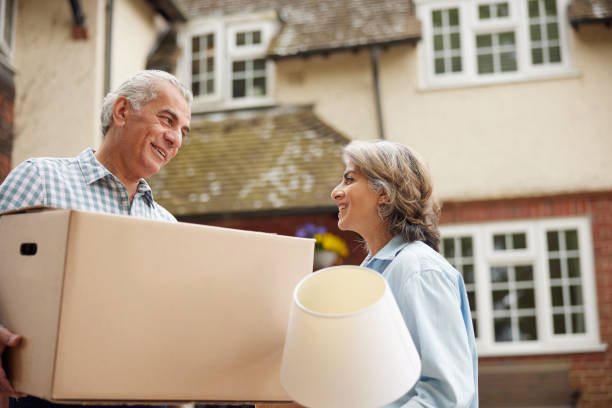 mature couple carrying boxes on moving day in front of dream home - downsizing imagens e fotografias de stock