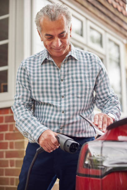 mature man attaching charging cable to environmentally friendly zero emission electric car at home - old men car vertical imagens e fotografias de stock