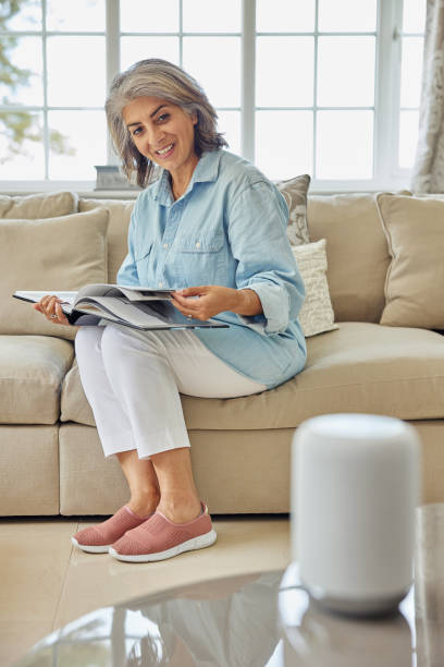 istock Mature Woman Sitting On Sofa Asking Digital Assistant Or Smart Speaker Question 1326037798
