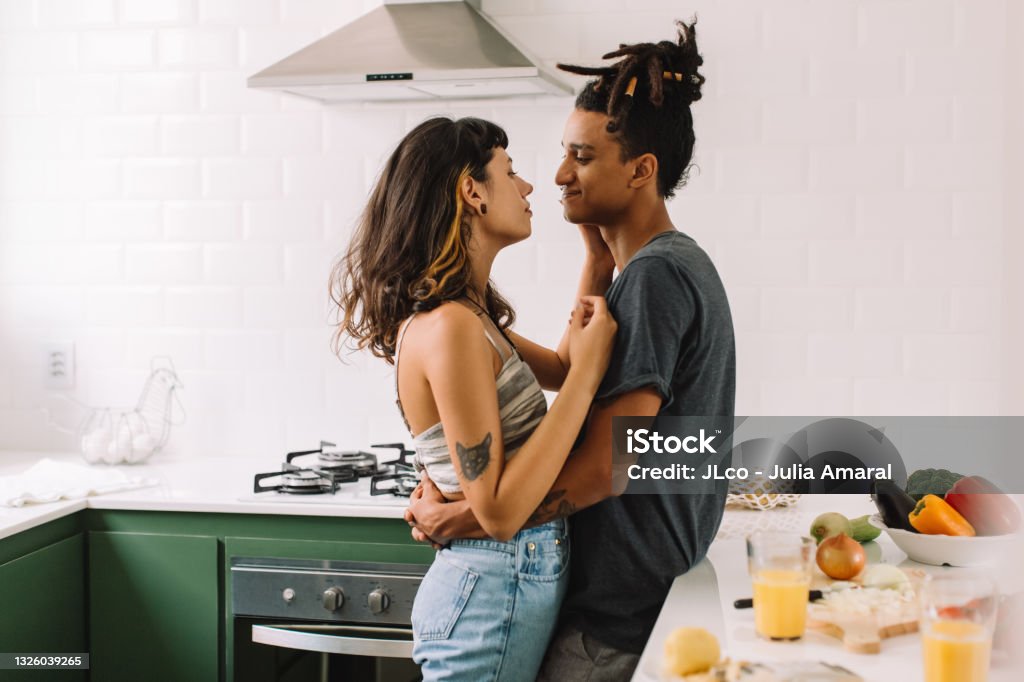 Beautiful young couple bonding in the kitchen Beautiful young couple bonding in the kitchen. Cropped shot of an affectionate young couple embracing each other while standing together in their kitchen. Couple sharing a romantic moment at home. Love - Emotion Stock Photo