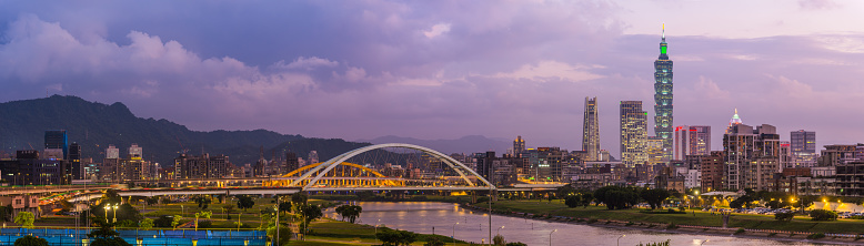 Panoramic view across the Keelung River to the glittering high-rise cityscape, skyscrapers in the heart of Taiwan’s vibrant capital city at dusk.