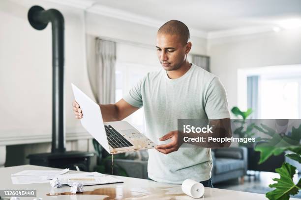Shot Of A Young Businessman Holding A Laptop Damaged By Coffee At Home Stock Photo - Download Image Now