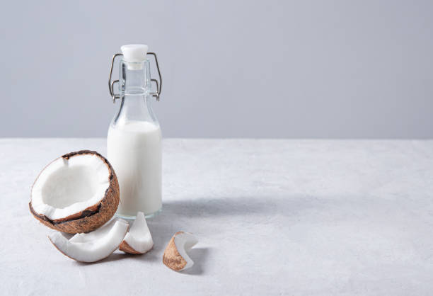 istock Glass vegan milk bottle on white marble table with half coconuts. Front view and copy space 1326049128