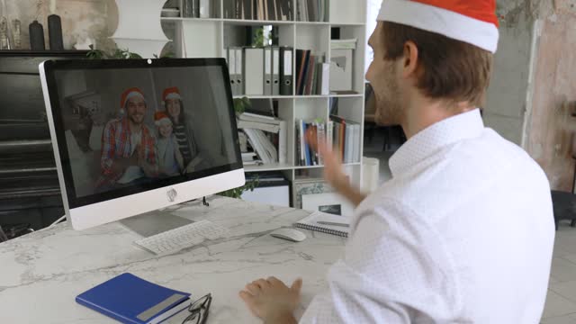 Handsome caucasian male having a video call with friends or colleagues on Christmas eve in office. Holidays celebration during COVID-19 Coronavirus isolation lockdown.