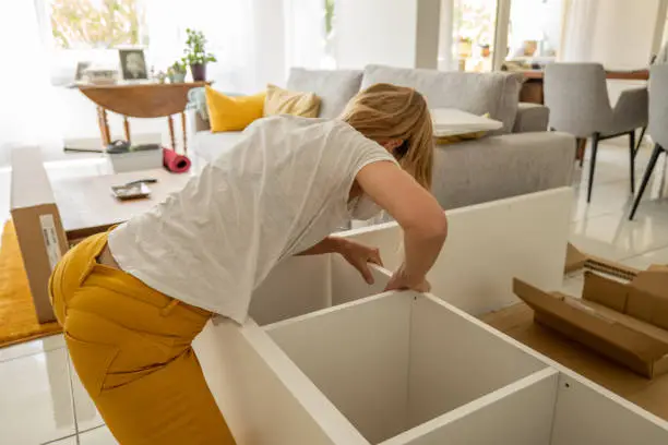 Young woman putting up flat pack furniture in his new home.
Woman Assembling Wooden Cabinet in Home 
Woman assembling wardrobe for his new home