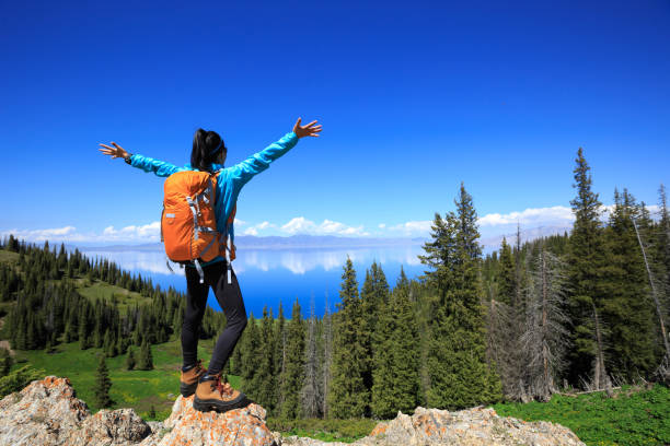 Successful woman backpacker hiking on forest mountain peak