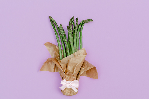 Creative spring concept as a top view shot of asparagus bouquet with kraft paper on a purple background.