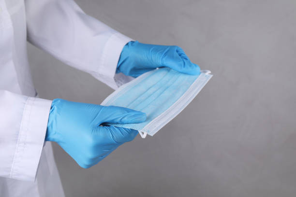 istock Doctor holding protective mask on light grey background, closeup 1326064163