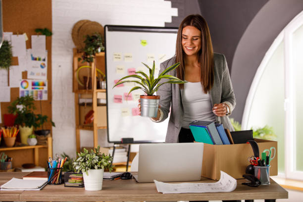 cheerful businesswoman unpacking at her new desk after getting hired - finishing employment issues occupation downsizing imagens e fotografias de stock