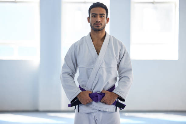 ritratto ritagliato di un bel giovane artista marziale maschio in piedi con le mani sulla cintura in palestra - purple belt foto e immagini stock