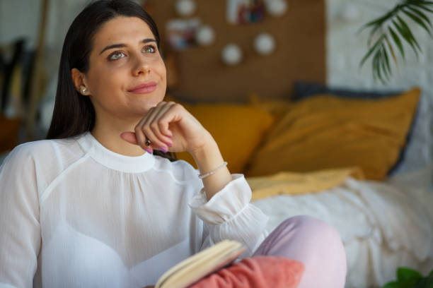 istock Young woman looking up and reminiscing about her day while writing in a diary 1326068755
