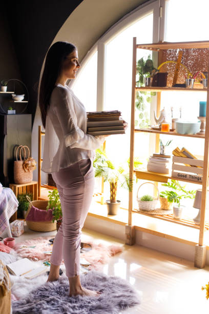 istock Young woman carrying stack of books toward a bookshelf 1326069552