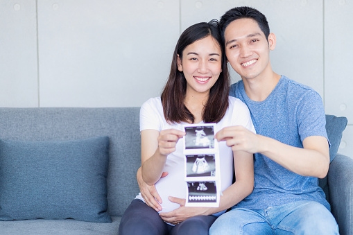 Pregnant woman and father showing baby ultrasound images.