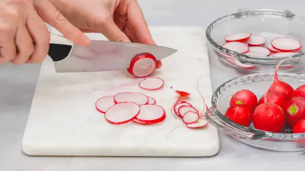 Photo of Fresh sliced radish close up on marble cutting board on light grey background. Vegetable salad preparation process, recipe