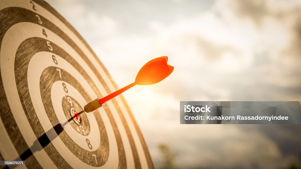 Close up shot red darts arrows in the target  of dartboard center on dark blue sky background. Business target or goal success and winner concept. Sports Target Stock Photo