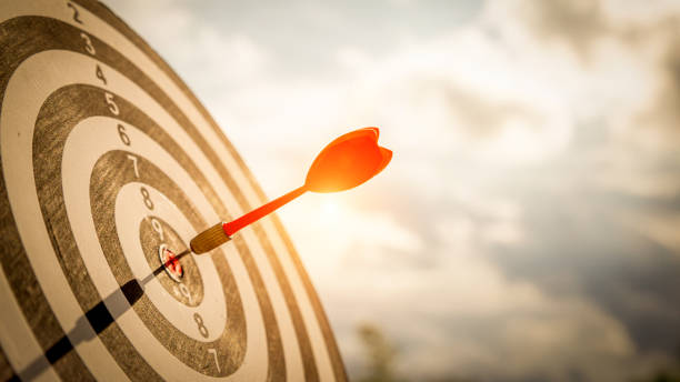 Close up shot red darts arrows in the target  of dartboard center on dark blue sky background. Business target or goal success and winner concept. Close up shot red darts arrows in the target  of dartboard center on dark blue sky background. Business target or goal success and winner concept. goal sports equipment stock pictures, royalty-free photos & images