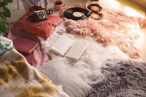 Copy space shot of abundance of fake fur rugs, vinyl records, analog camera, books and an open diary arranged on a bedroom floor.