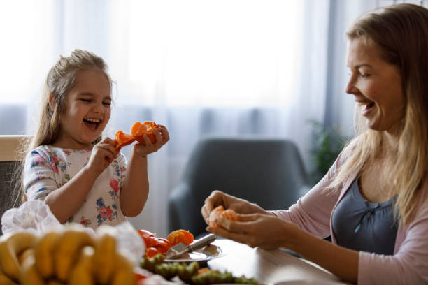 Little girl having fun peeling tangerines with her mother while making a fruit platter