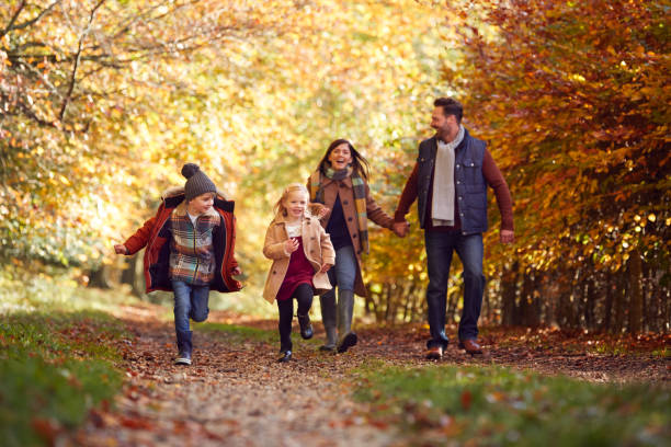 familia caminando por la pista en el campo de otoño con niños corriendo por delante - correr fotos fotografías e imágenes de stock