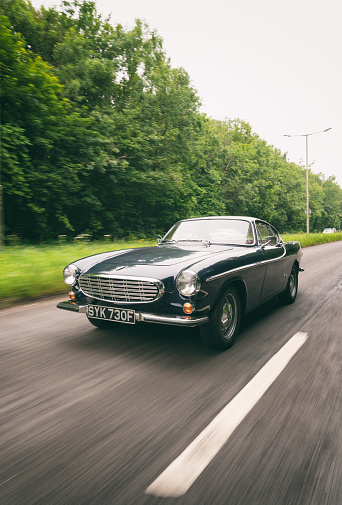Buckinghamshire, UK - June 28, 2021: A classic dark blue Volvo 1800S from 1967 speeding down a road in the south east of England. Made famous when a white version was used by Roger Moore in the iconic sixties tv show The Saint, this svelt Swedish sports coupe is still a head-turner to this day.