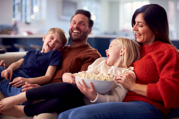 istock Family Sitting On Sofa With Popcorn Laughing Watching Comedy On TV Together 1326079360