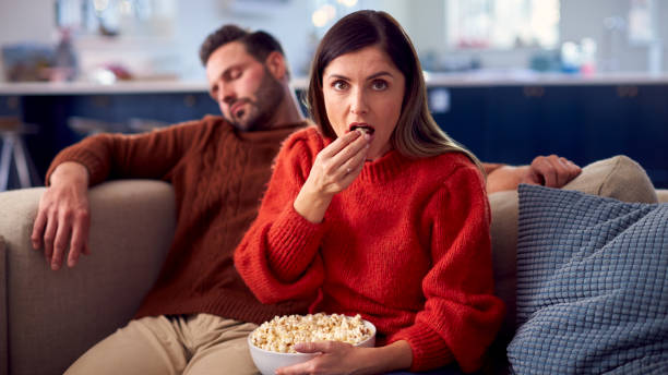 man falls asleep as couple sit on sofa with popcorn watching tv - date night imagens e fotografias de stock