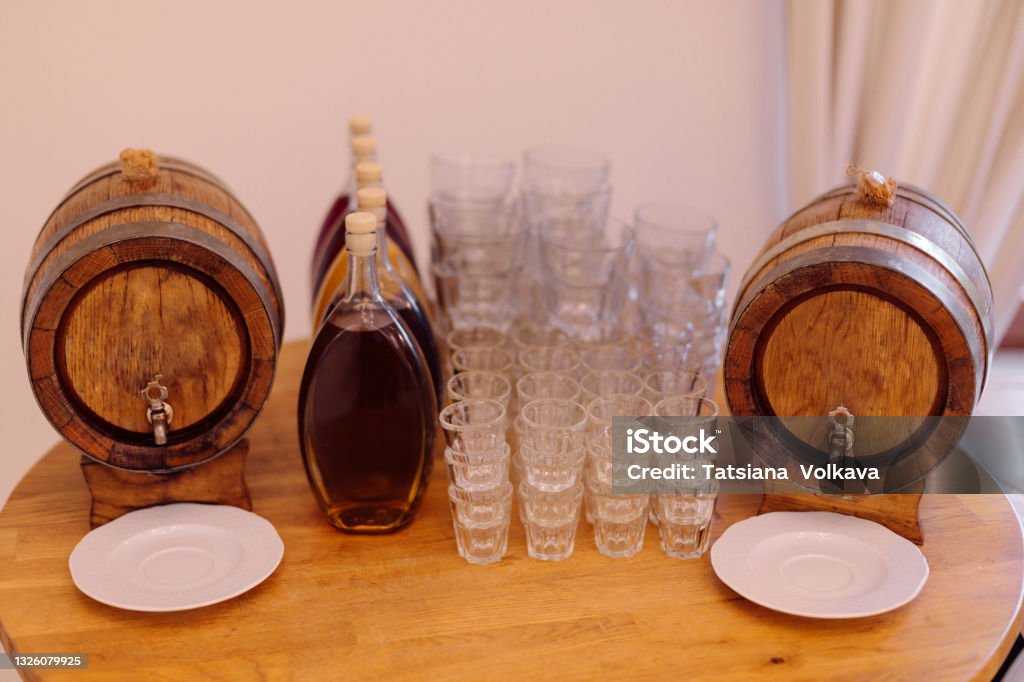 Two barrels of local traditional alcoholic beverages and several glass glasses are prepared for tasting on round wooden table. Recreation and travel. Festive events. National cuisine and drinks. Two barrels of local traditional alcoholic beverages and several glass glasses are prepared for tasting on round wooden table. Recreation and travel. Festive events. National cuisine and drinks. Strong alcoholic surprise. Barrel Stock Photo