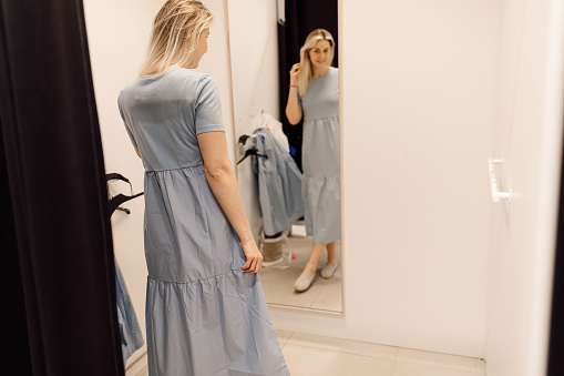 Beautiful blonde is in great mood during fitting of dress that suits her very well. Organization of sales process in supermarkets. Fashionable clothes. Shopping and pleasure. Convenience and comfort. Lifestyle.photo
