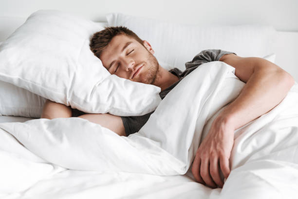 beau jeune homme dormant dans son lit - supine photos et images de collection