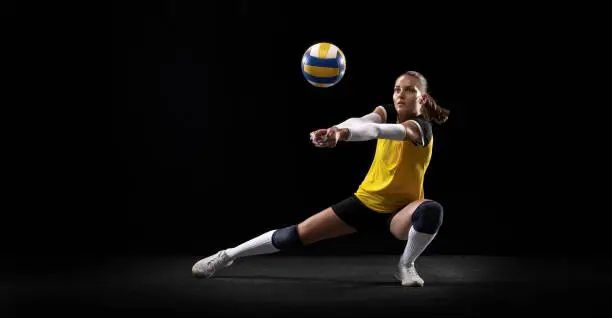 Game in defense. Female professional fit volleyball player with ball isolated on black studio background. The athlete, exercise, action, sport, training, fitness concept. The girl in motion.