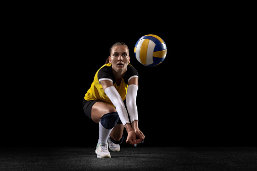 Game in defense. Female professional fit volleyball player with ball isolated on black studio background. The athlete, exercise, action, sport, training, fitness concept. The girl in motion.