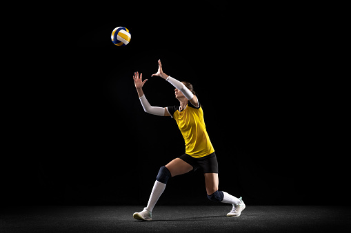 Female professional passer volleyball player with ball isolated on black studio background. The athlete, exercise, sport, healthy lifestyle, training, fitness concept. The girl in motion in striker kick