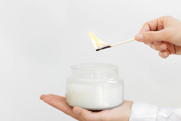 womans hand uses match to light aromatic candle in glass jar with natural ingredients on white background. - fire match women flame imagens e fotografias de stock