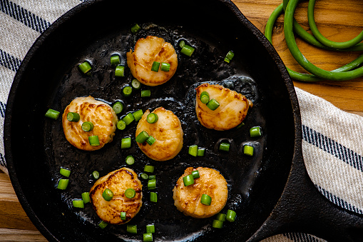 Scallops seared in a cast-iron pan with butter and garlic scapes.