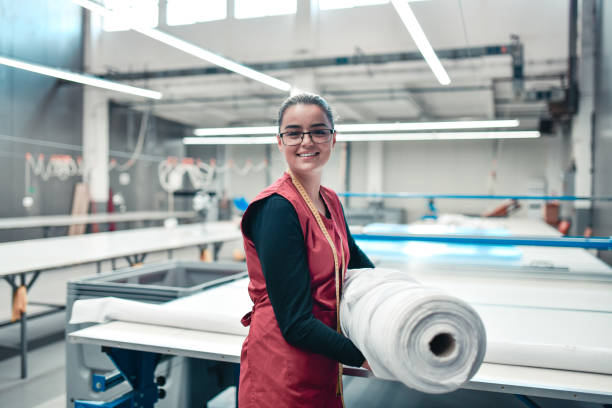 lavoratrice sorridente che trasporta materiali laminati pesanti per la stampa di macchine a rulli - industria tessile foto e immagini stock