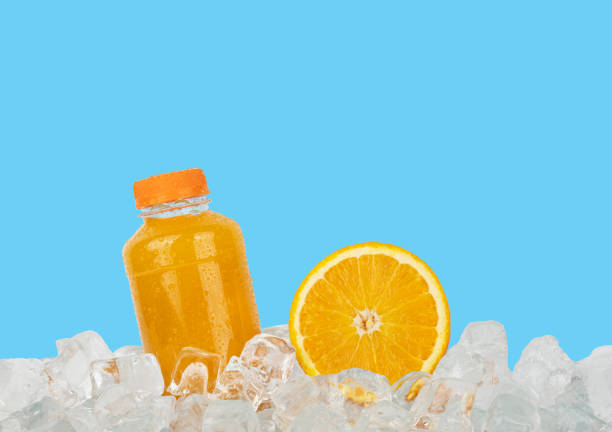 Close up one plastic PET bottle full of fresh orange juice and cut half orange slice on ice cubes isolated on blue background, low angle side view