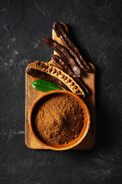 istock Carob bean and powder on board flat lay on black background 1326099010