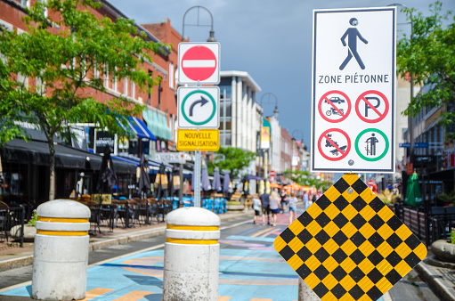 Road signs on pedestrian street with people walking on Des Forges Street after rain during day of summer in Trois-Rivieres