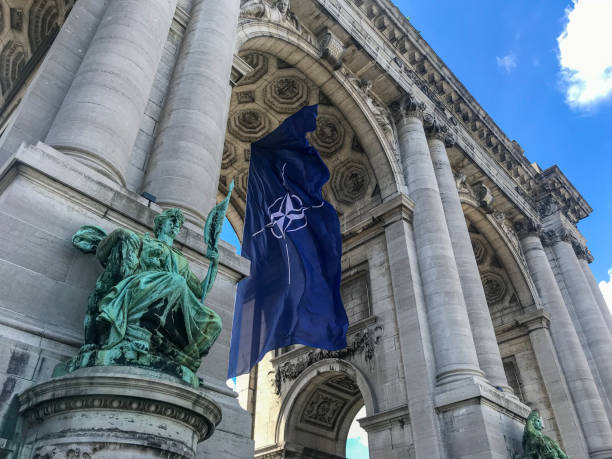 NATO flag between the arcades of the Cinquantenaire BRUSSELS, BELGIUM - JUNE 14, 2021: NATO flag fluttering in the wind in the arcades of the Cinquantenaire in Brussels nato stock pictures, royalty-free photos & images