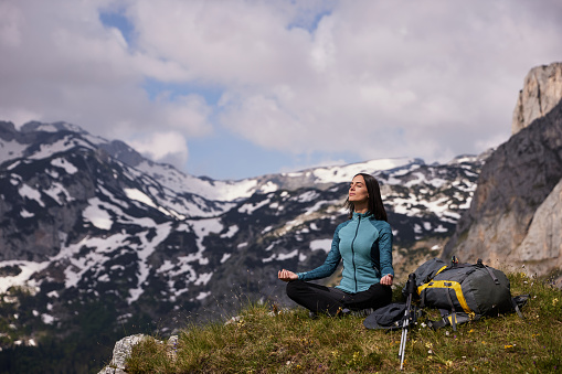 Female hiker with backpack relaxing and meditating at mountain peak