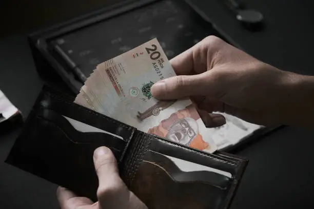 Male hands piking up 20000 Colombian pesos banknotes of a wallet on a dark office