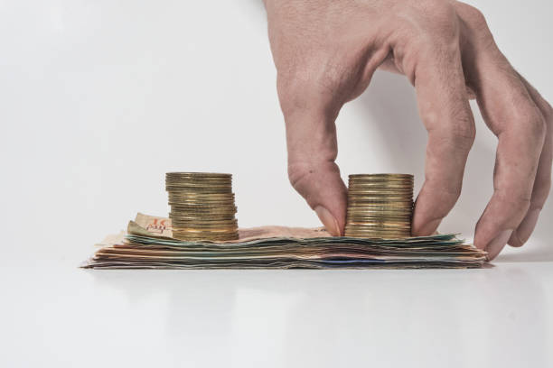 istock hand picking up coins over a pile of banknotes on a white background 1326108077