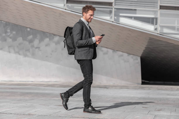 행복한 젊은 사업가는 도시 거리에서 배낭 가방과 함께 일하기 위해 통근 통근에 전화를 사용하여. 스마트 폰을보고 사업가 문자 메시지 - blazer men suit business 뉴스 사진 이미지